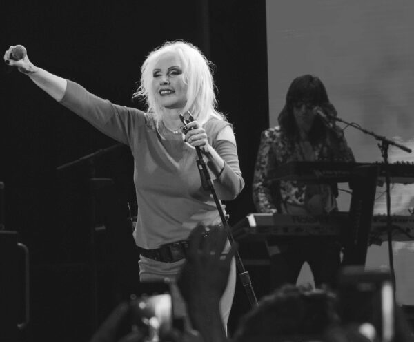Debbie Harry, pevačica grupe Blondie, tokom koncerta u londonskom Roundhouseu 2017. godine, u crvenoj haljini, sa mikrofonom i ispruženom rukom